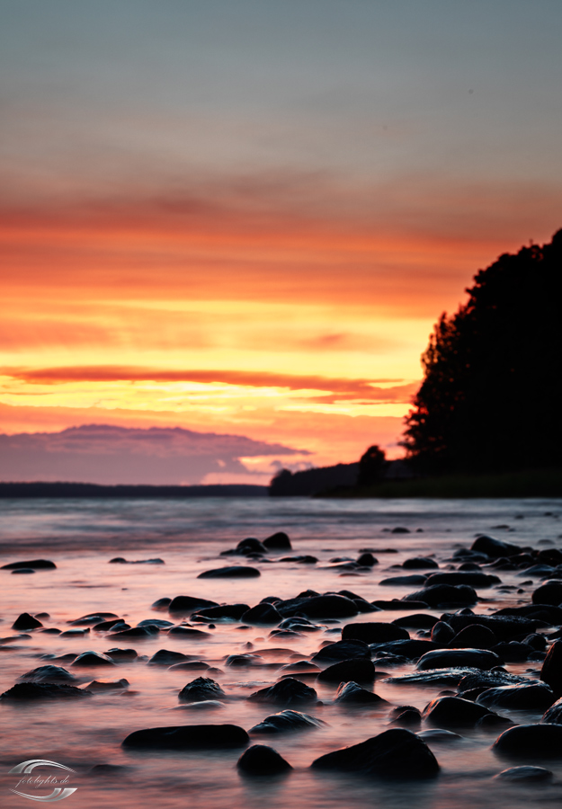 Abendrot an einem See mit Steinen im Vordergrund