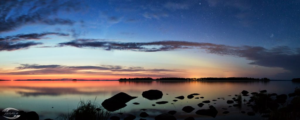 Panorama eines Sees am Abend mit dem Rest Abendrot am Horizont und Steinen im Vordergrund