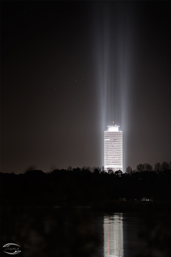 Ein sich im Wasser spiegelnder beleuchteter Turm bei Nacht