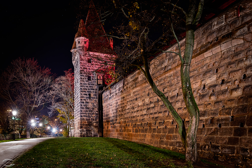 Blick entlang der Burgmauer auf einen rot angestrahlten Turm