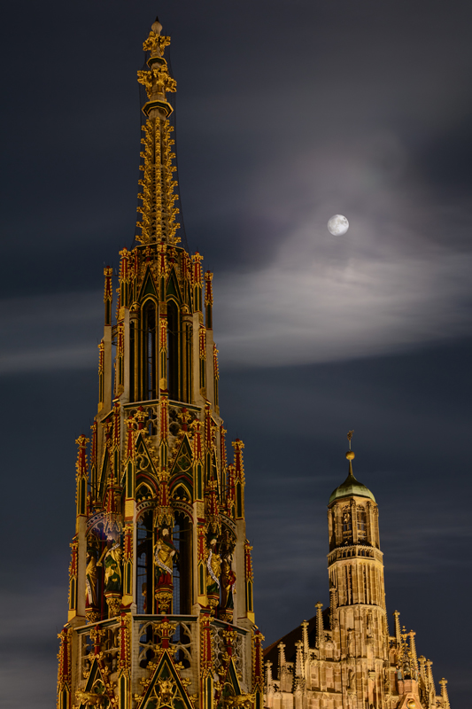 Schöner Brunnen und Frauenkirche mit Mond darüber bei Nacht