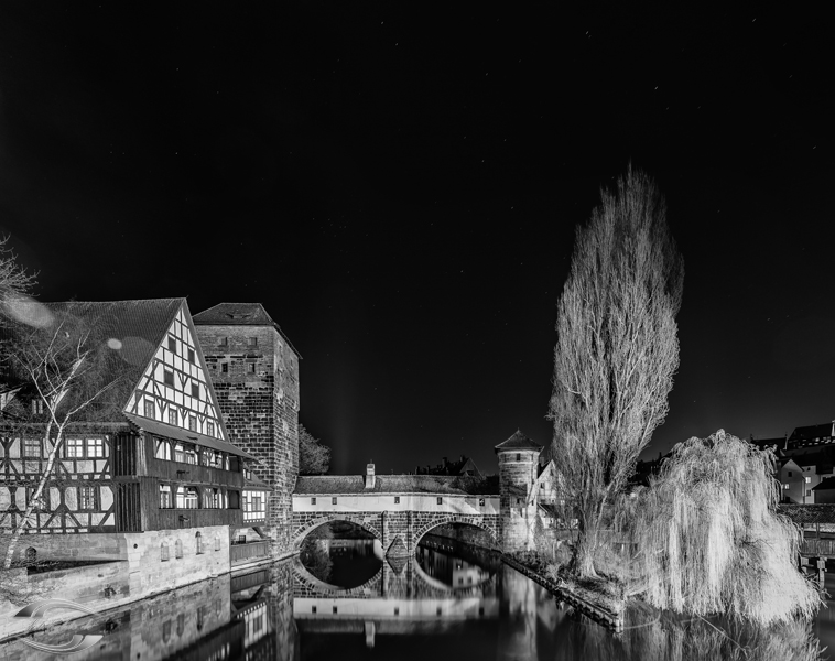 Schwarz-Weiß-Bild vom Weinstadl und zweier Bäume an einem Fluss bei Nacht